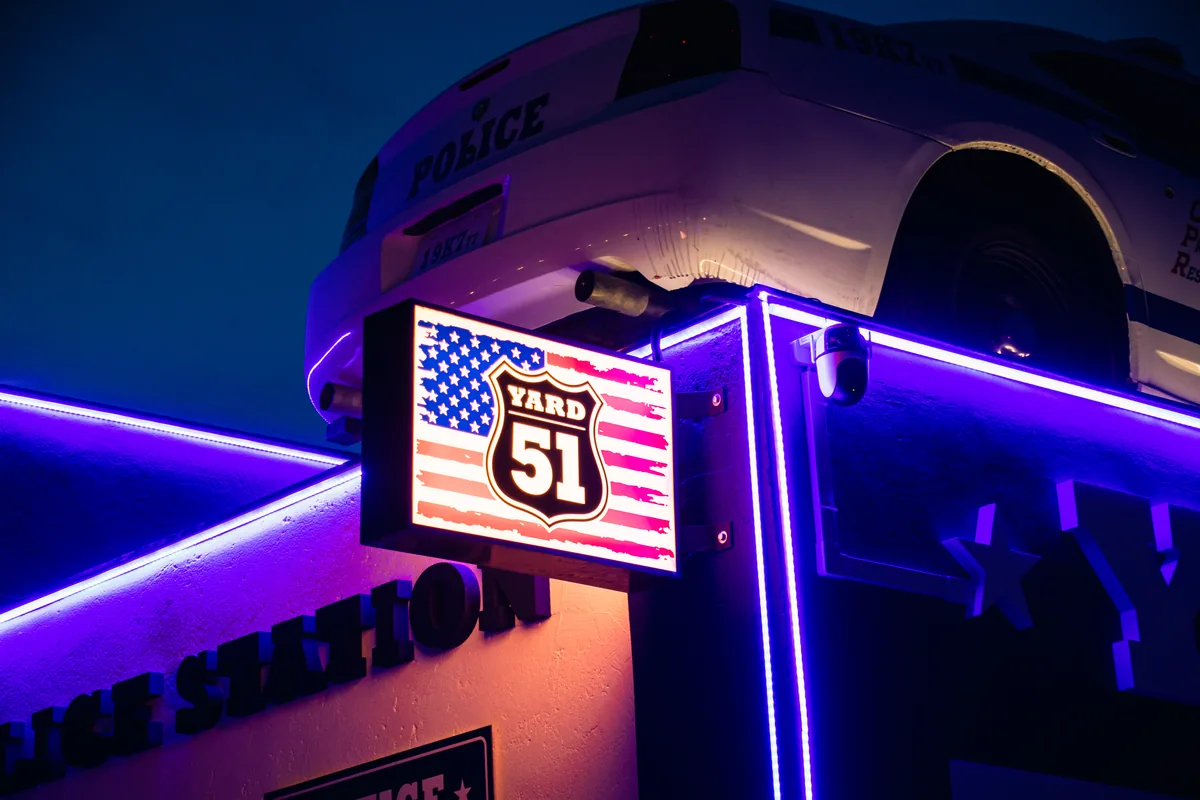 A YARD 51 neonfényes homlokzata és a tetőn álló rendőrautó éjszaka